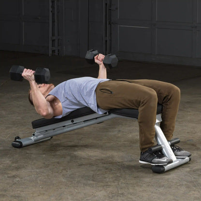 Man performing dumbbell bench press on an incline bench wearing brown pants in a gym.
