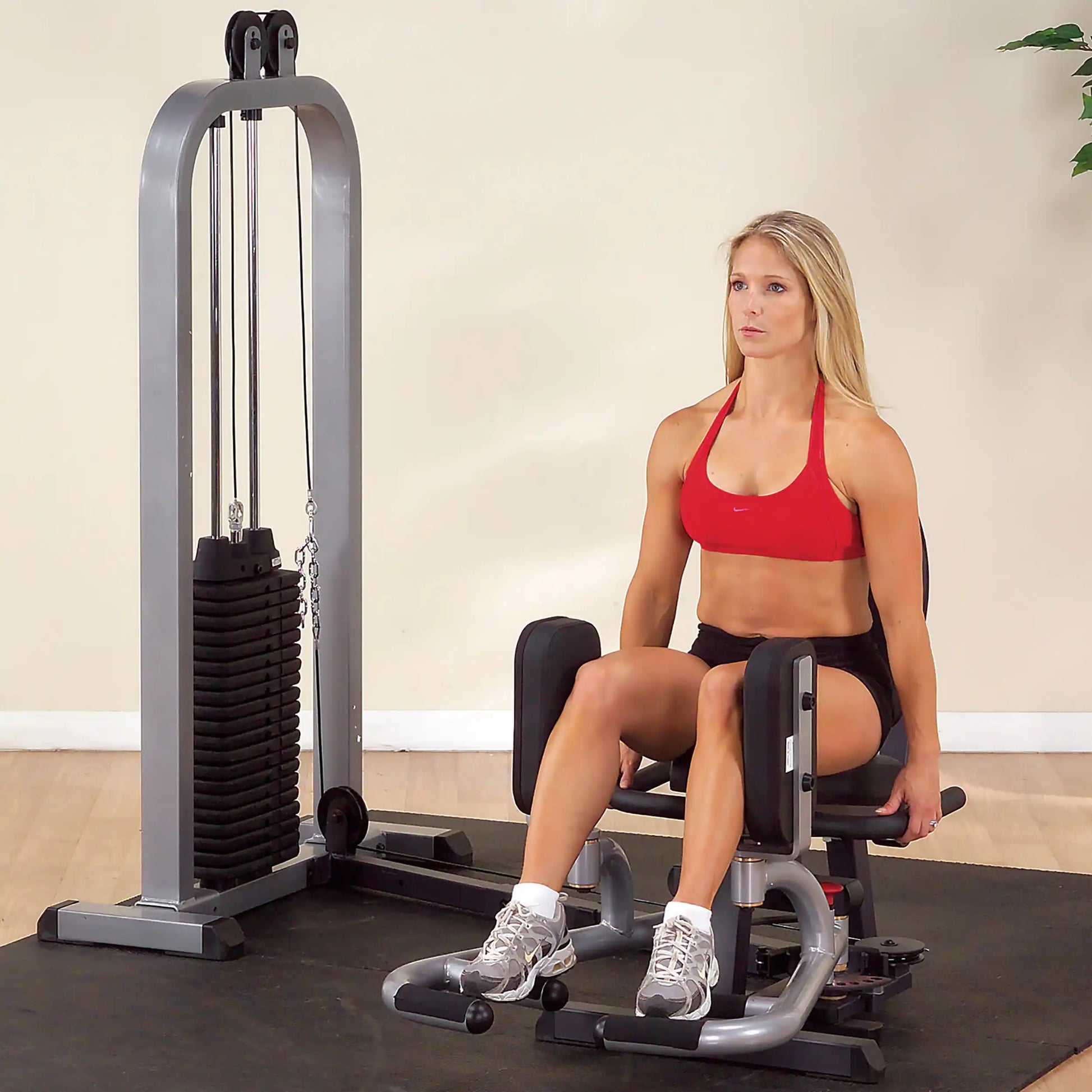 Woman using a Body-Solid inner thigh machine in a gym.
