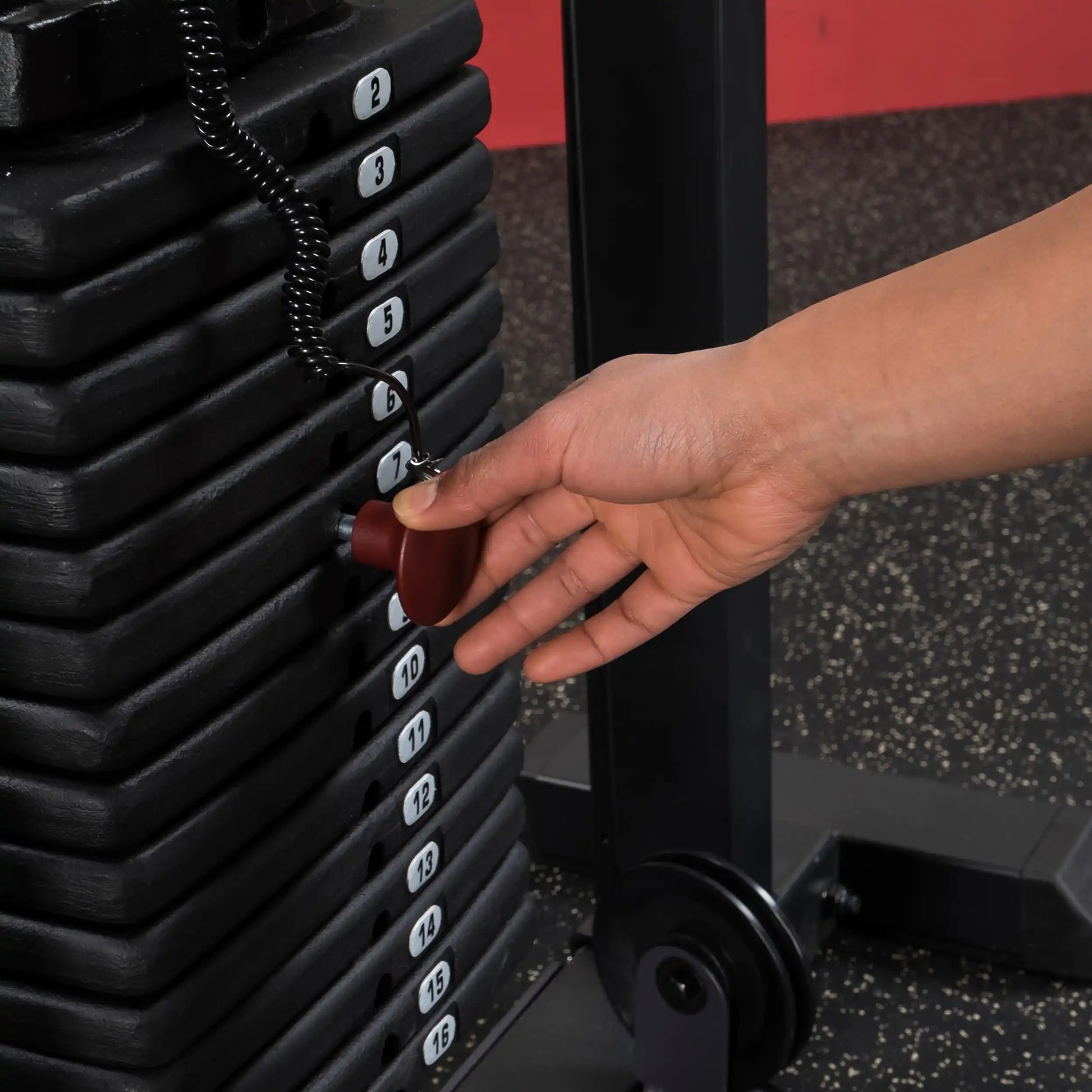 Hand adjusting weight selector pin on black gym machine stack for customized workout.