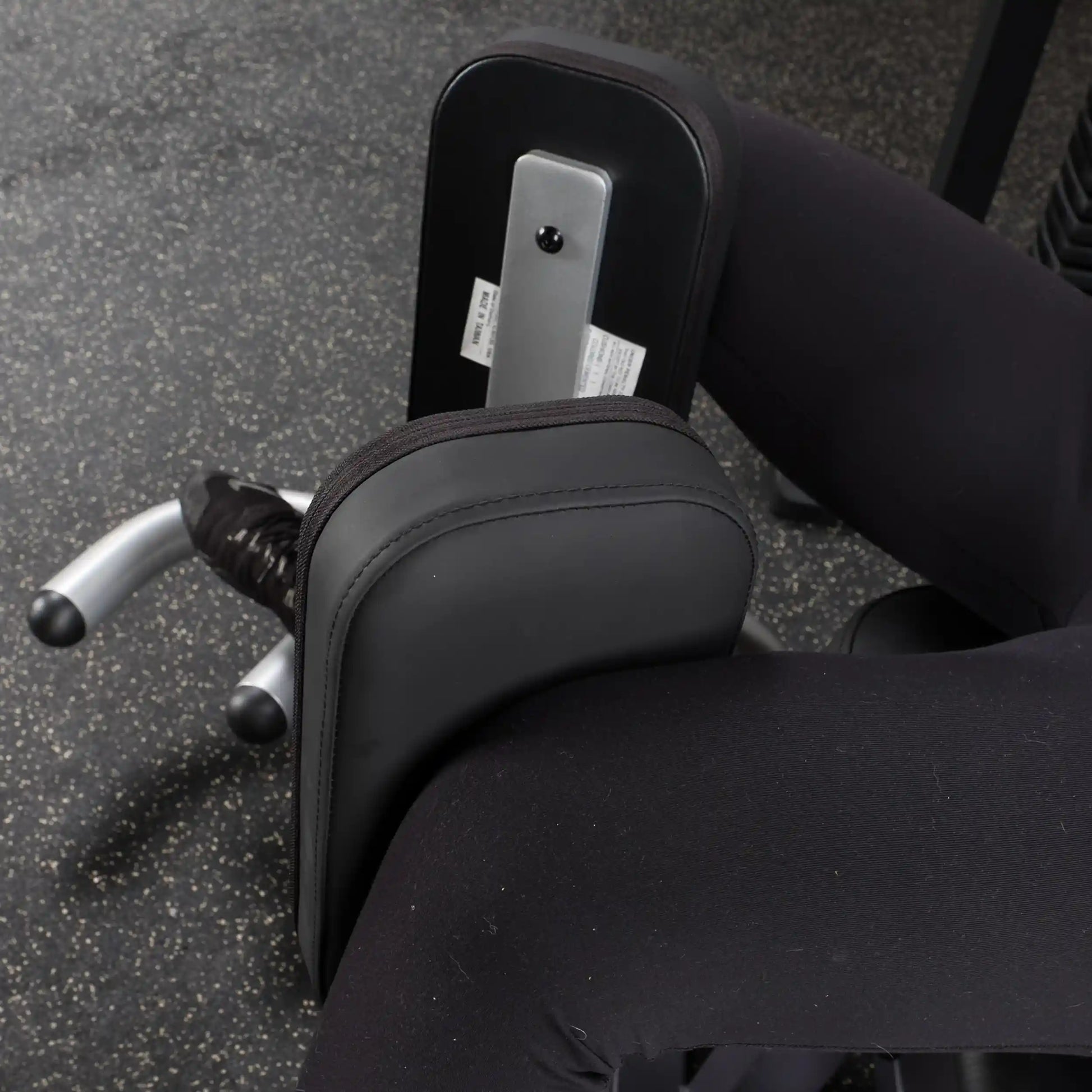 Legs using a black leg press machine with padded support in a gym.