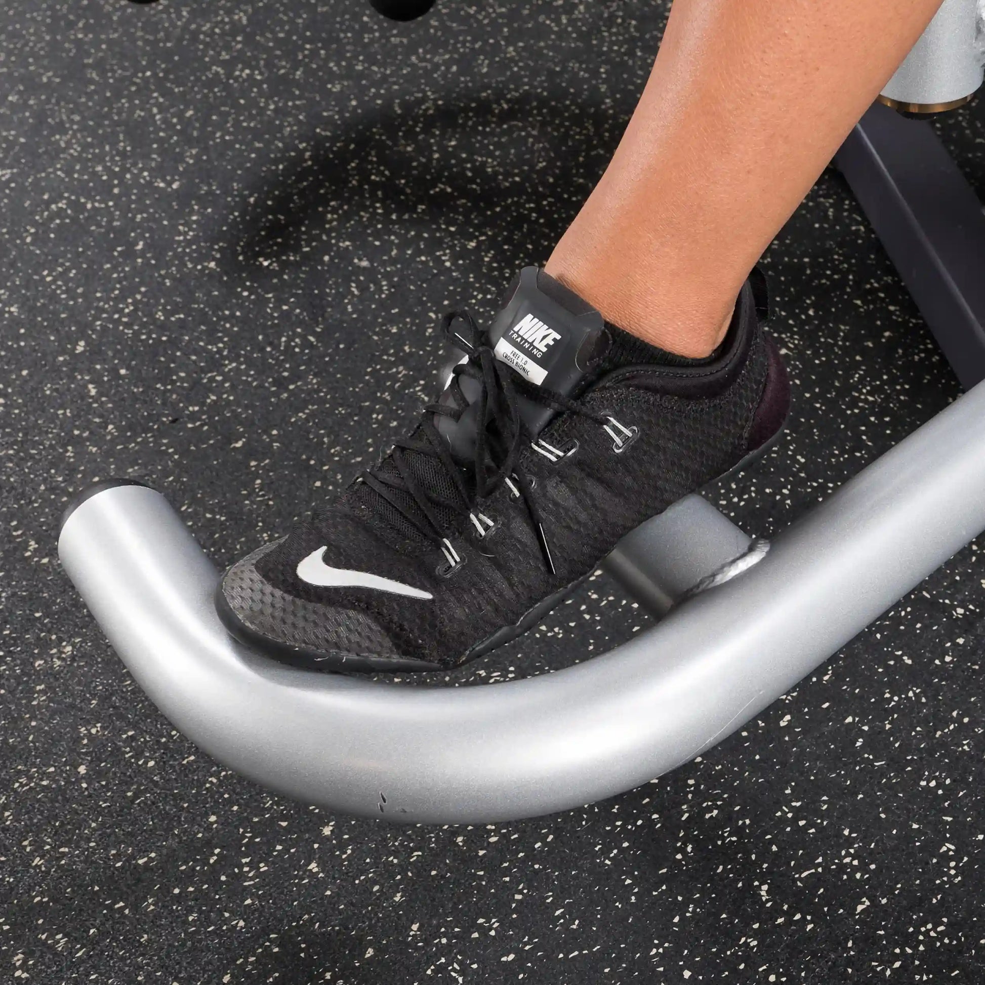Nike black sneaker on gym machine footrest, showcasing workout footwear.