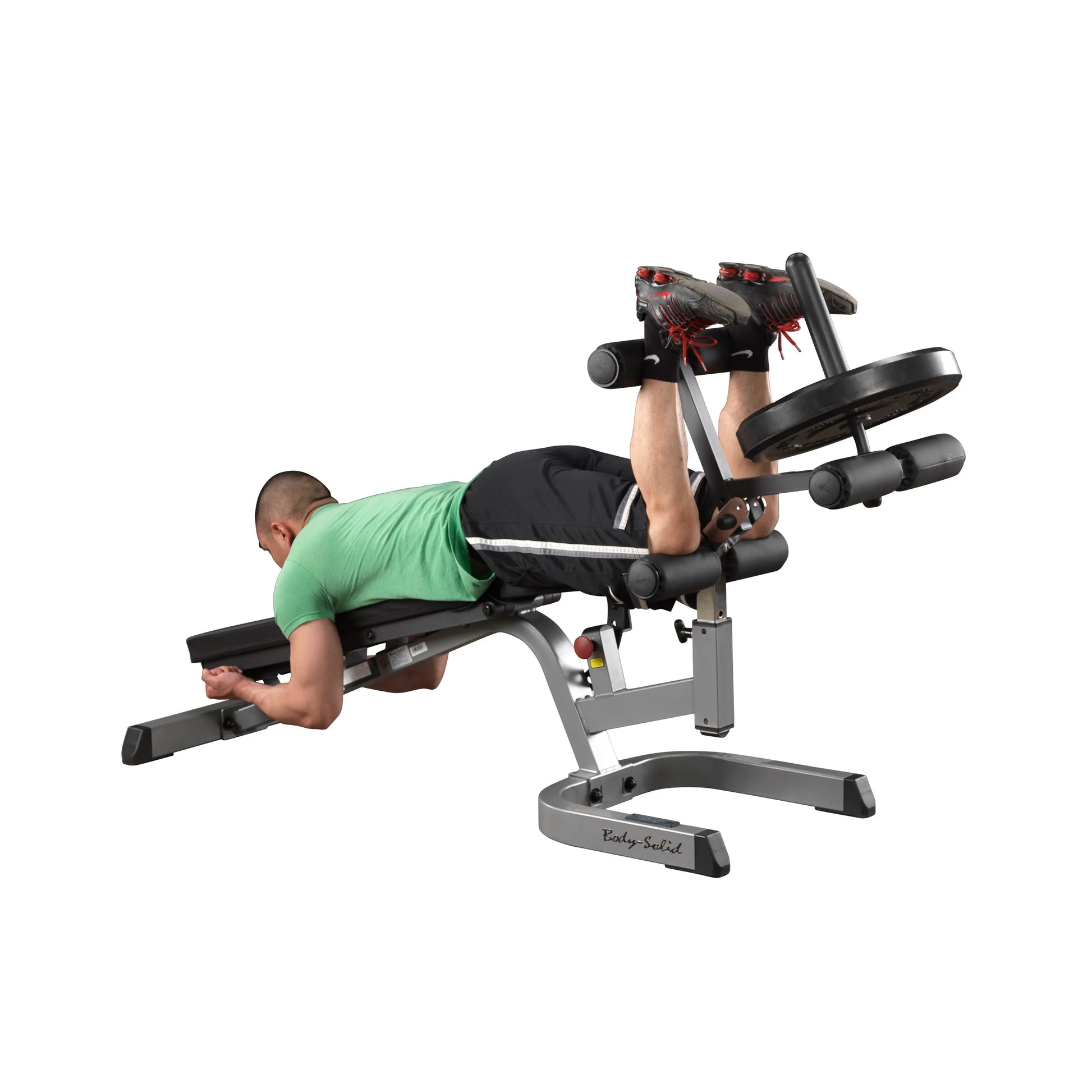 Man using Body-Solid leg curl machine with weights, wearing green shirt and black shorts.