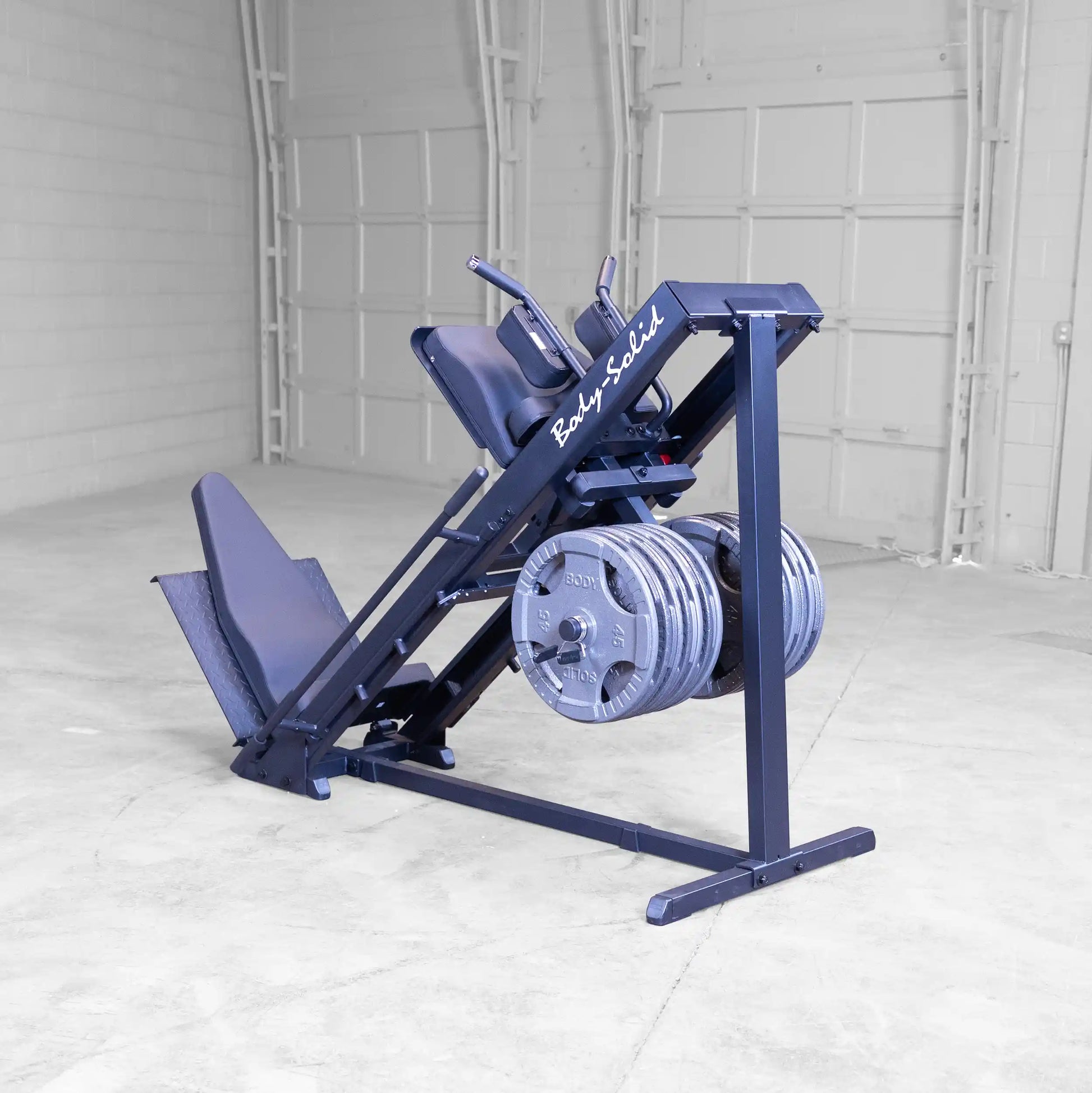 Body-Solid leg press machine with weights, featuring black padded seats in a spacious gym setting.