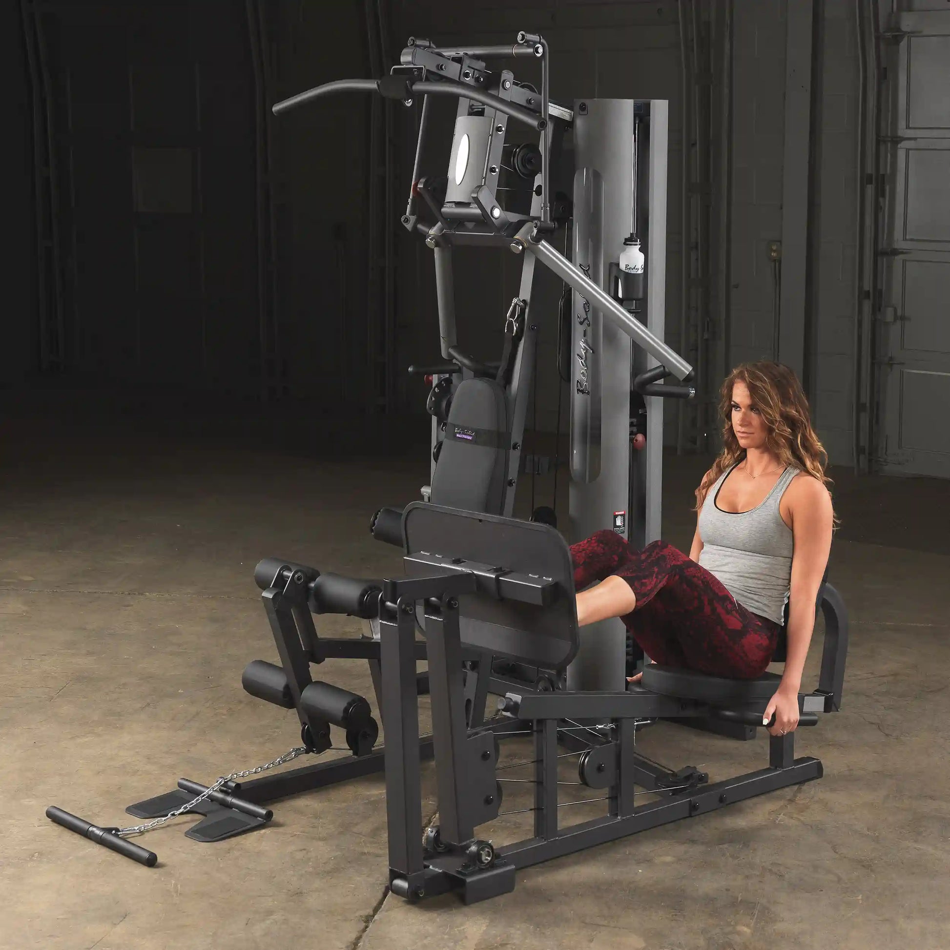 Woman using Body-Solid home gym machine for leg exercises in workout space.