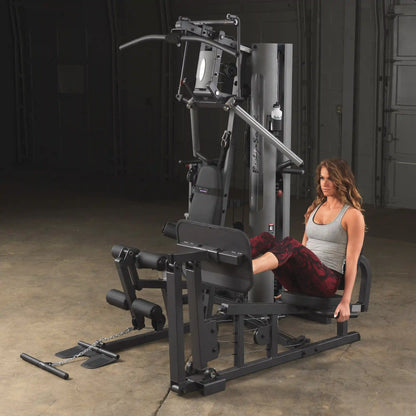 Woman using Body-Solid home gym machine for leg exercises in workout space.