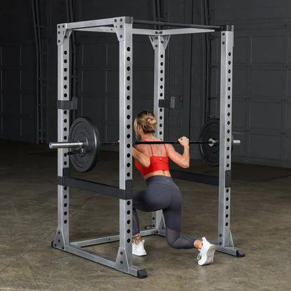 Woman performing squat in power rack, wearing red sports top and gray leggings.