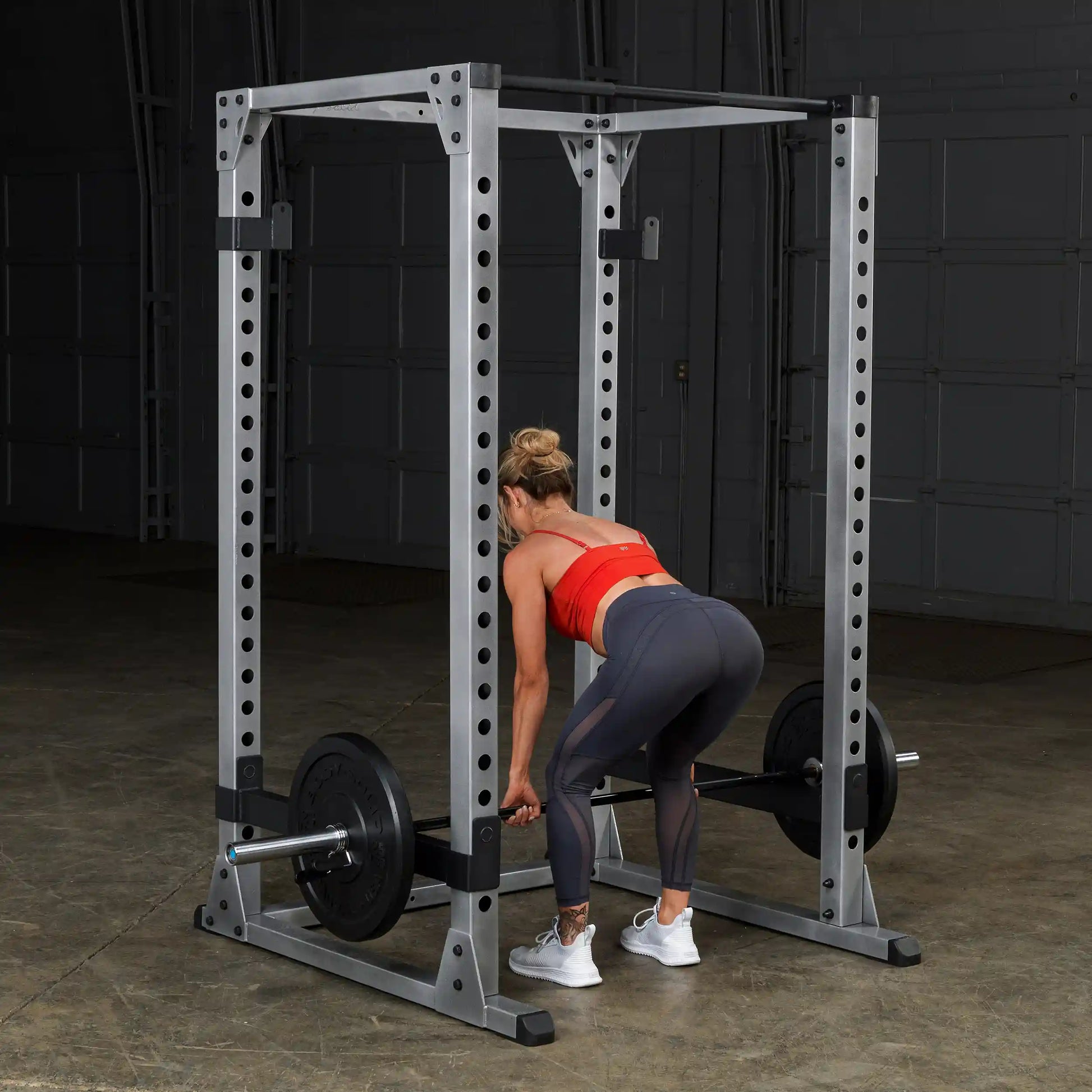 Woman lifting weights in a power rack, wearing a red top and gray leggings.