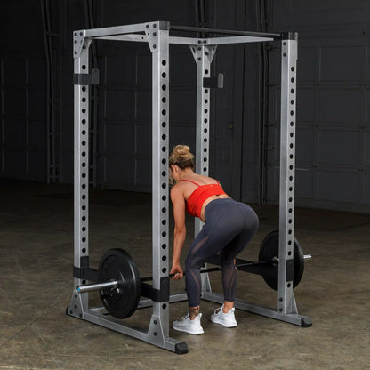 Woman lifting weights in a power rack, wearing a red top and gray leggings.