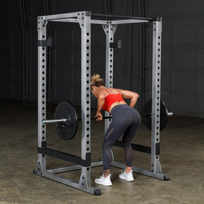 Woman lifting barbell in a power rack, wearing red top and leggings, demonstrating weightlifting exercise.