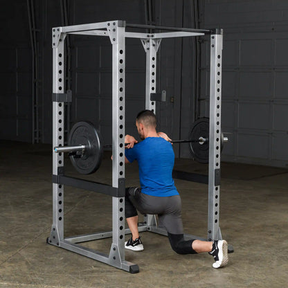 Man performing split squat in a power rack wearing blue shirt and black shorts.