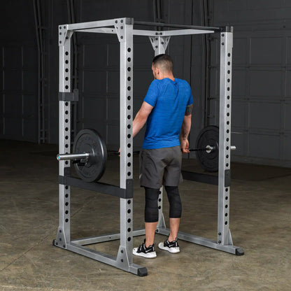 Man lifting weights in a Powerline squat rack, wearing a blue shirt and black knee sleeves.