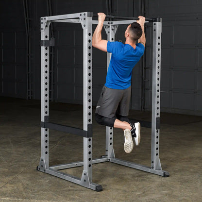 Man doing pull-up on steel power rack in gym, wearing blue shirt and black shorts.