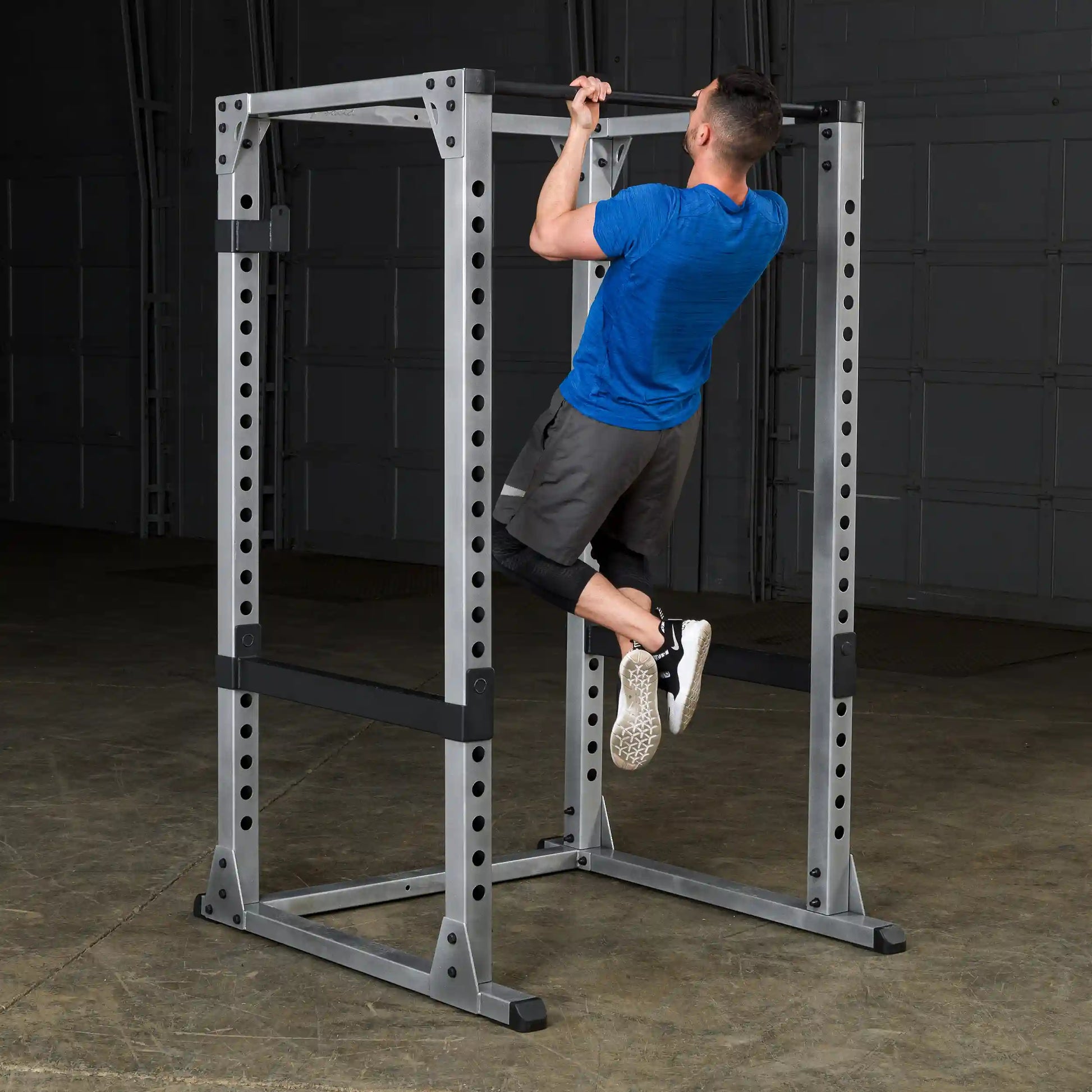 Man performing pull-up on steel power rack in gym.