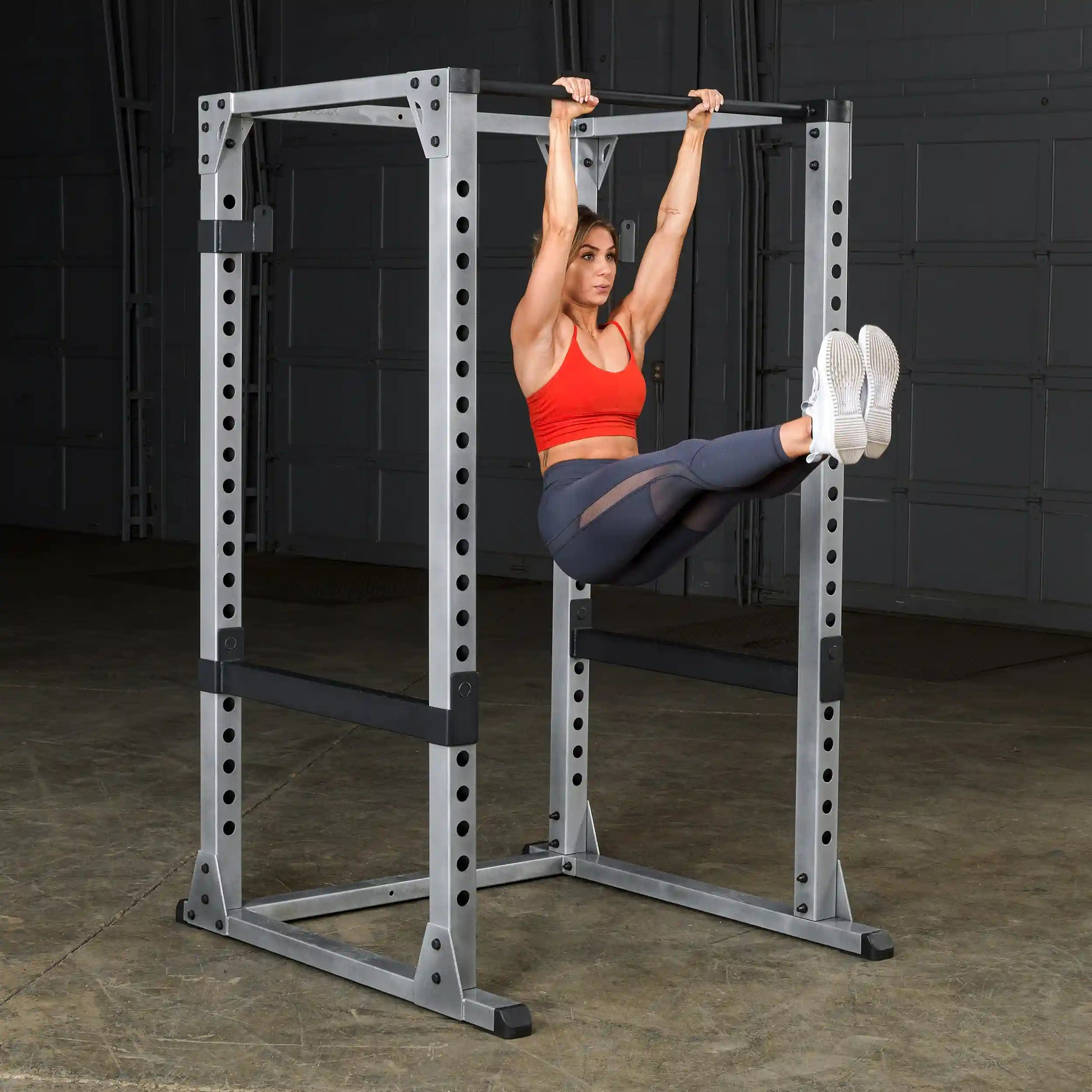 Woman performing leg raises on a power rack in a gym wearing a red sports bra.