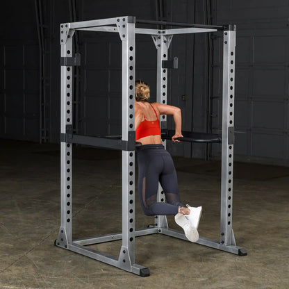 Woman using power rack for tricep dips in gym, wearing red sports bra and black leggings.