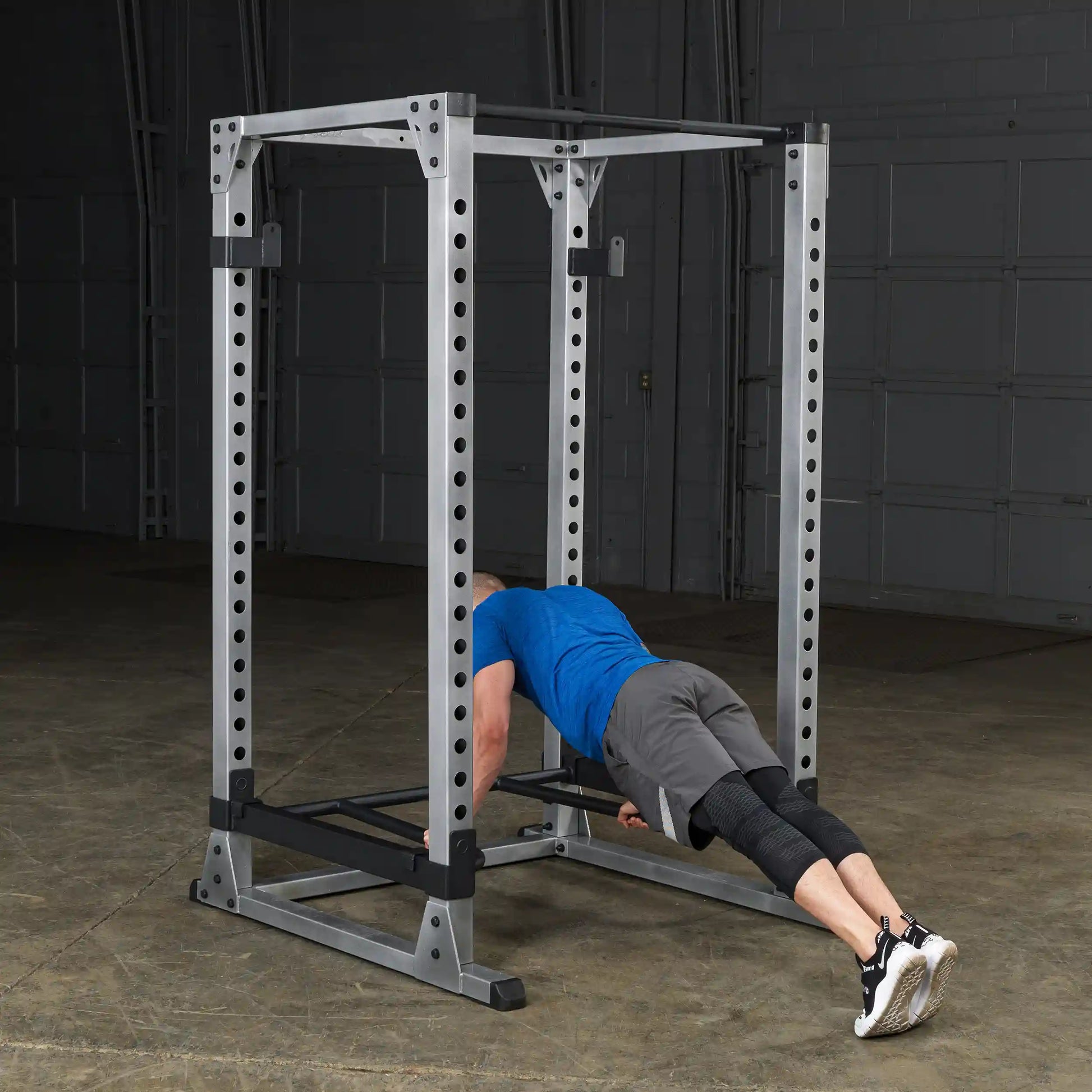 Man performing push-ups on Rogue power rack in blue shirt and black shoes.