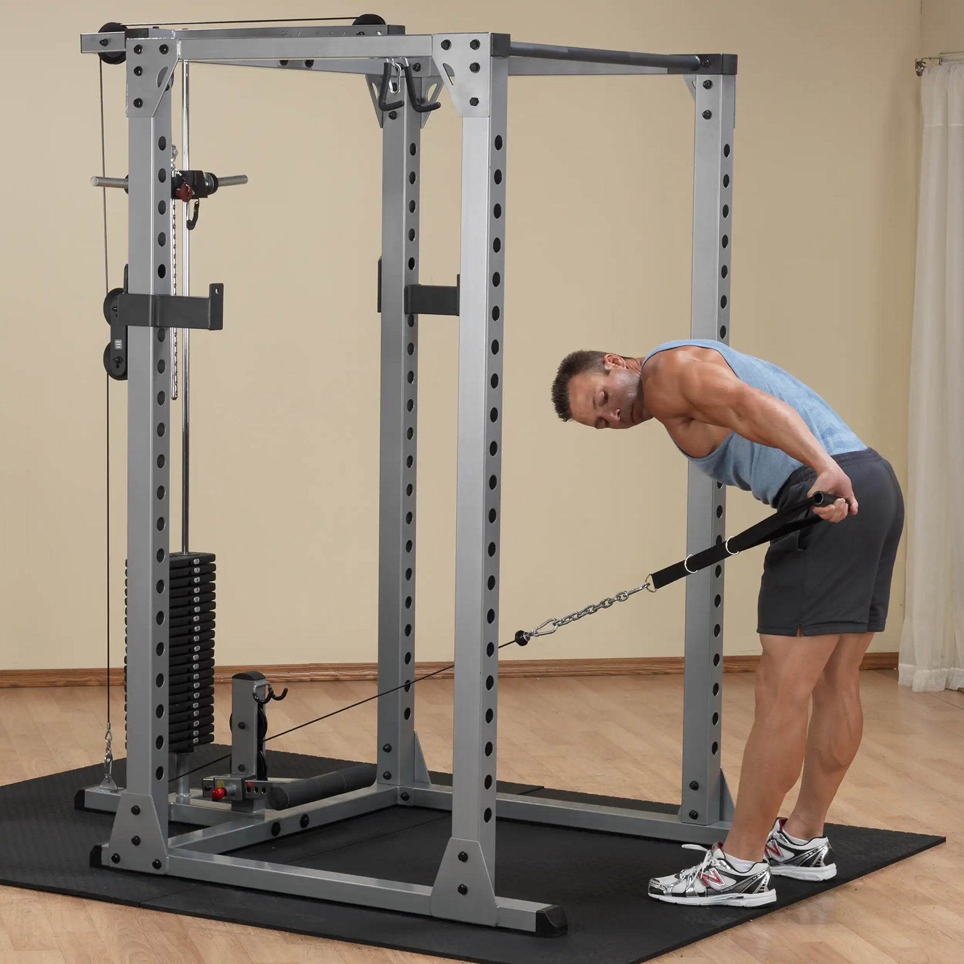 Man exercising with cable machine in gym, wearing blue tank top and gray shorts.