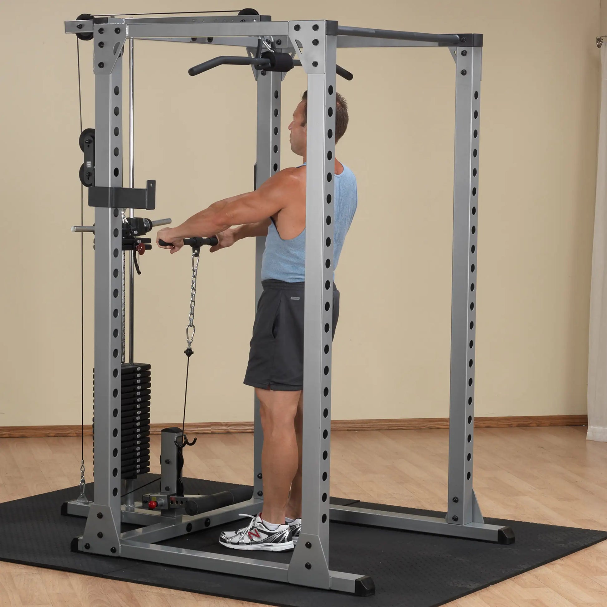 Man using a gray power rack for cable exercises in a home gym setup.