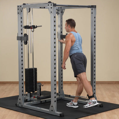 Man using a cable machine for leg exercises, wearing a blue tank top and shorts.