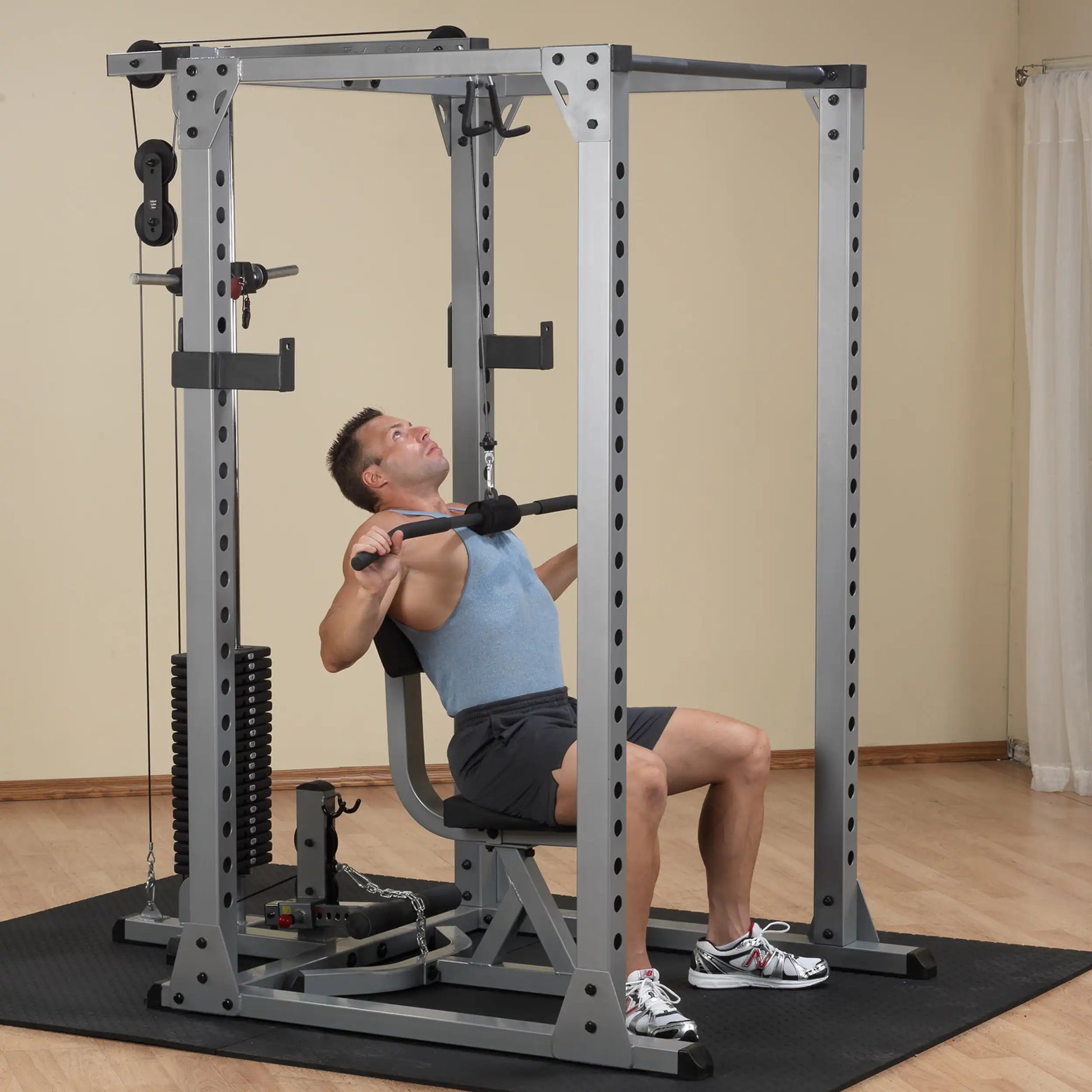 Man using a gray home gym machine for lat pulldowns, wearing a blue tank top.