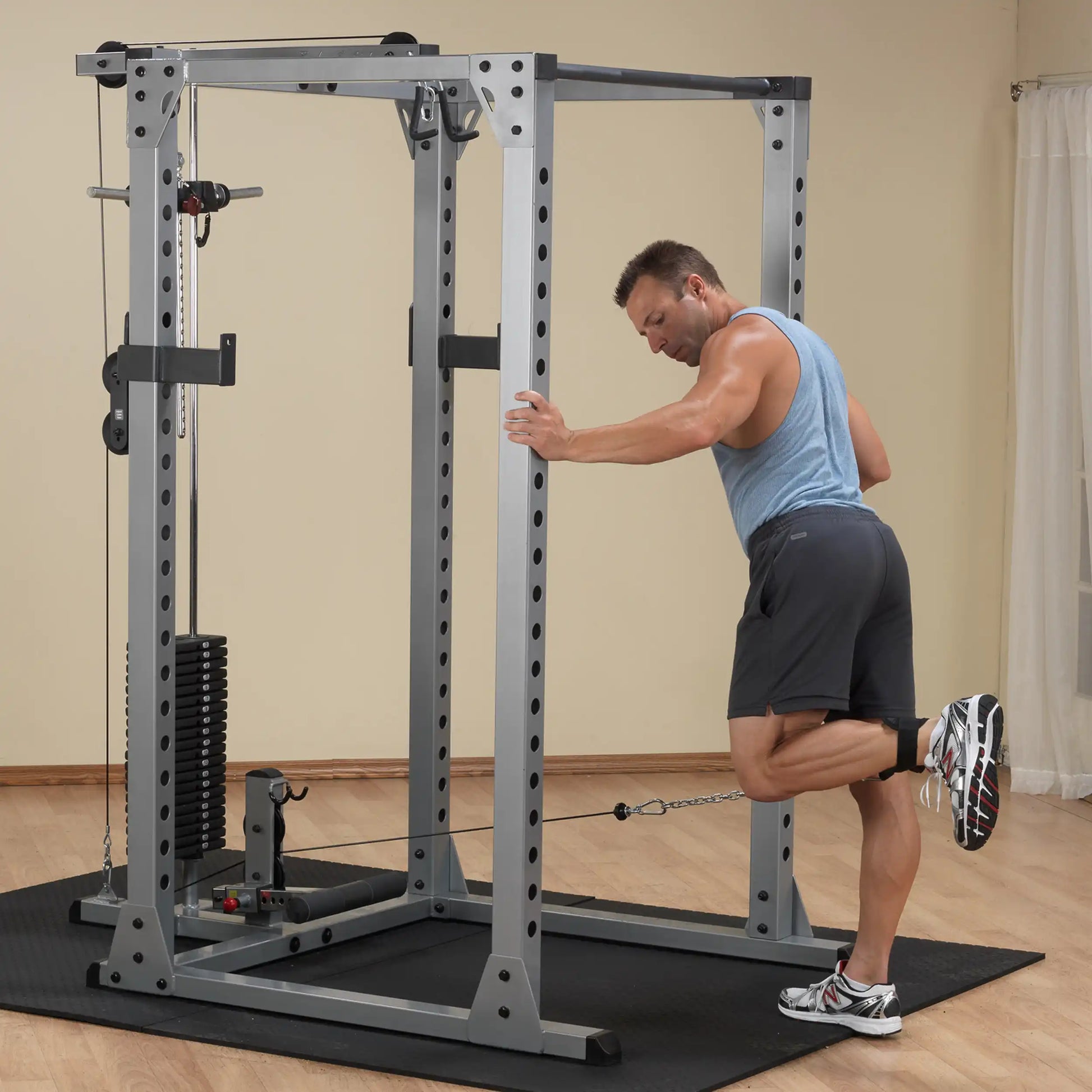 Man exercising with a cable machine in a home gym, wearing a blue tank top and black shorts.