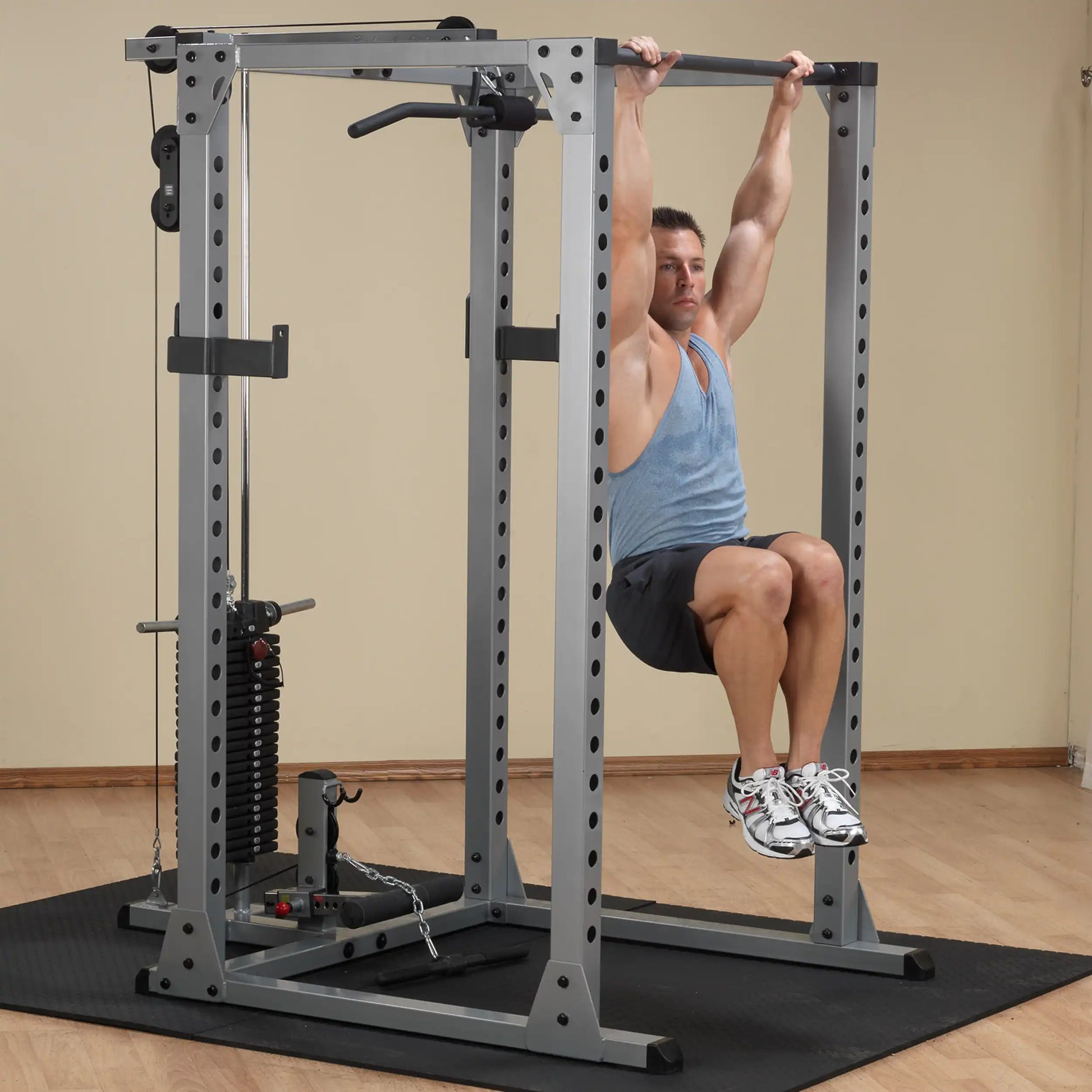 Man performing leg raises on a silver power rack, wearing a blue tank top and black shorts.