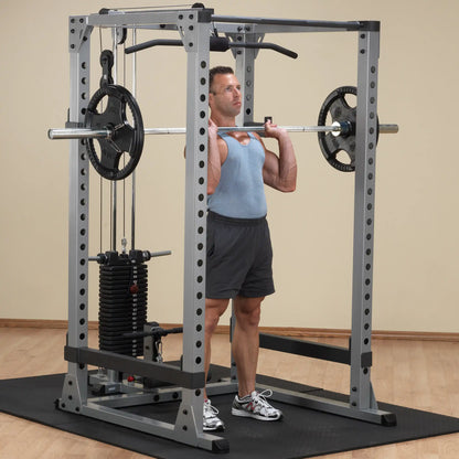 Man lifting barbell on Smith machine in gym, wearing blue tank top and gray shorts.