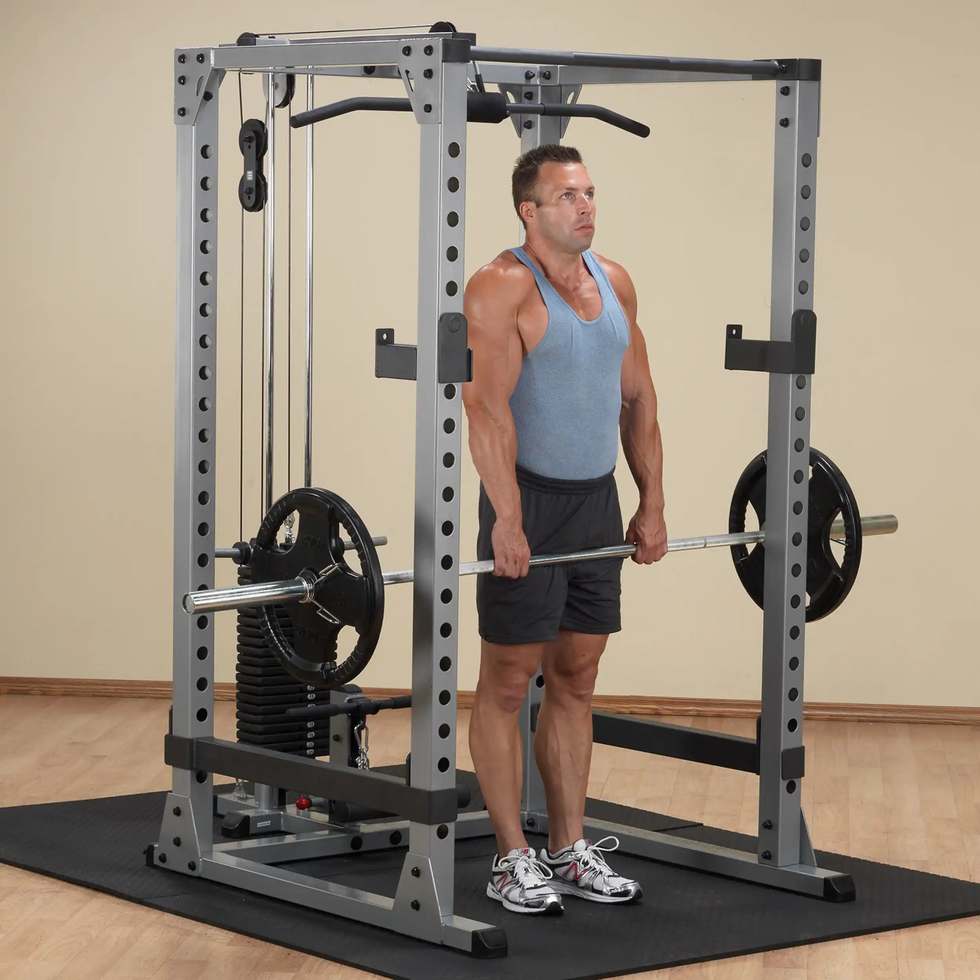 Man lifting weights on a gray power rack in a gym, wearing a blue tank top and black shorts.
