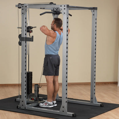 Man exercises on a steel power rack with cable attachments in a gym.
