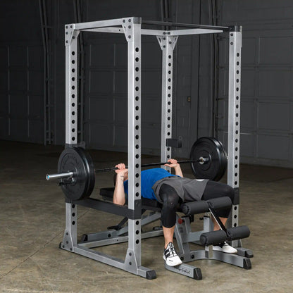Person bench pressing in Body-Solid power rack, featuring black weights, in a home gym setting.