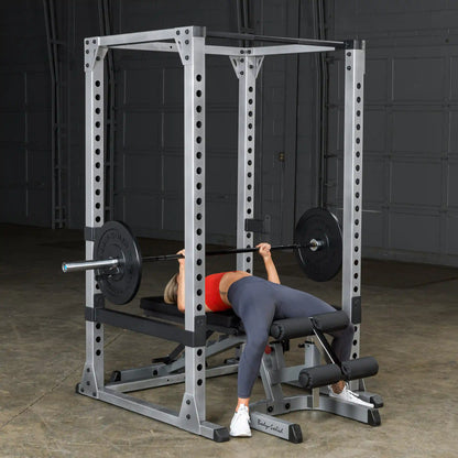 Woman performing bench press on Body-Solid power rack in a gym.