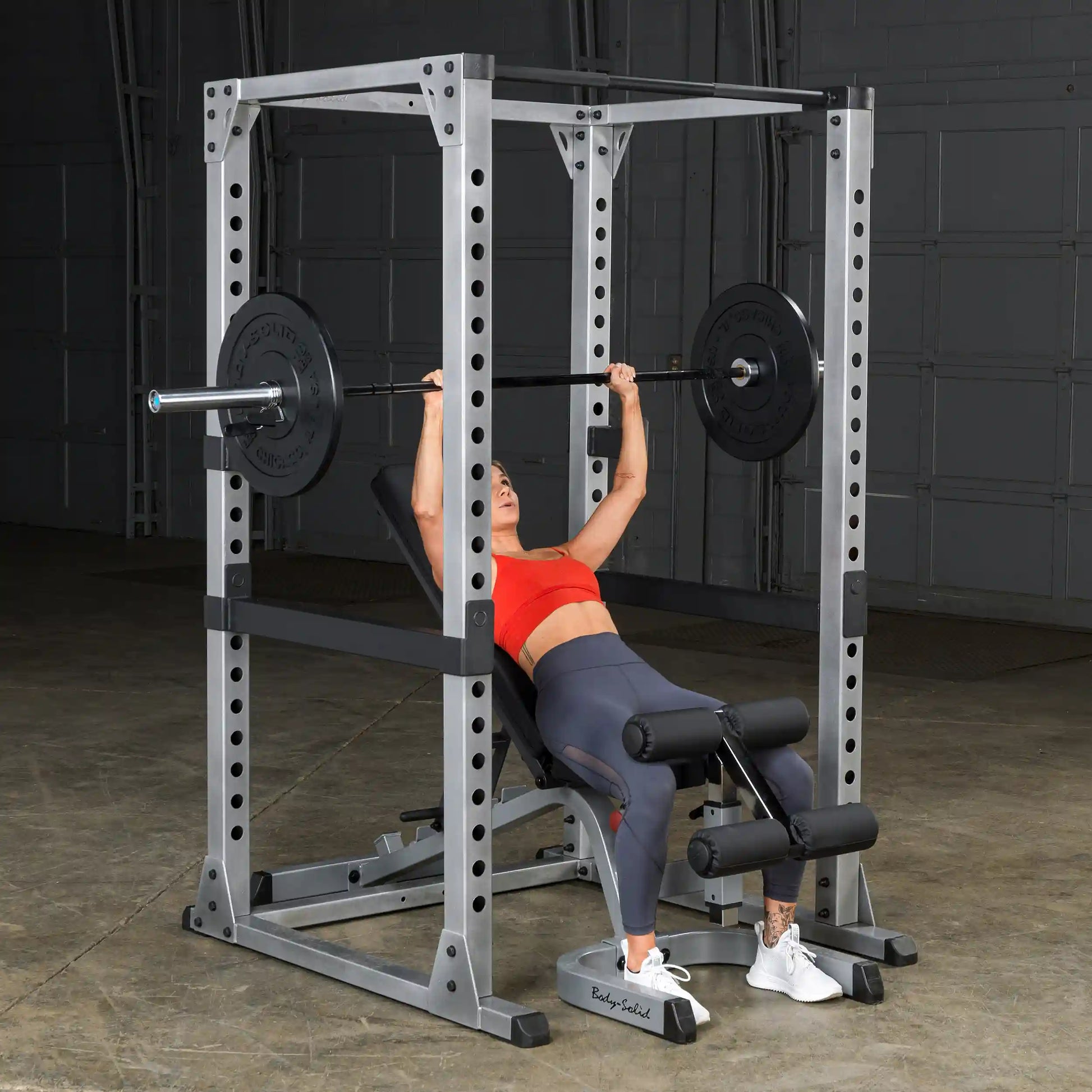 Woman bench pressing on Body-Solid power rack in red top and leggings.