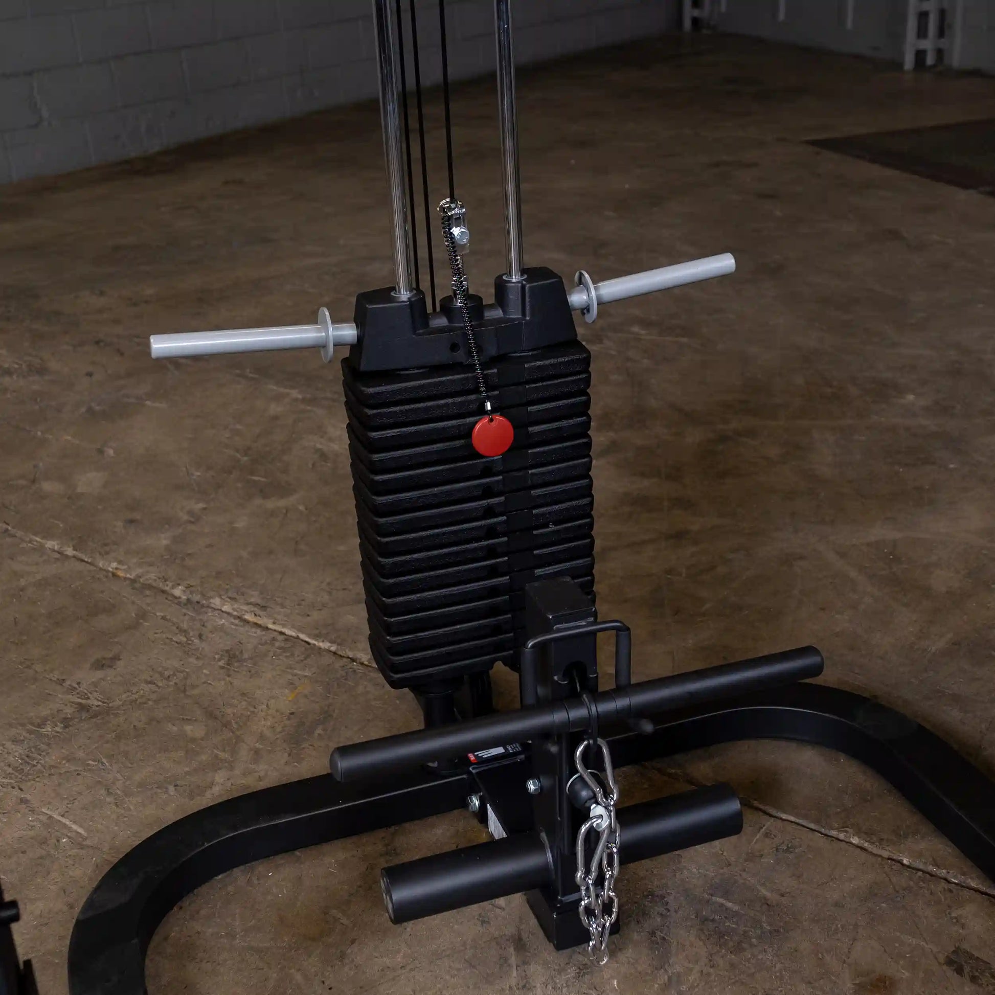 Gym weight stack with black plates and chrome rods, featuring a red selector pin for adjustable resistance.