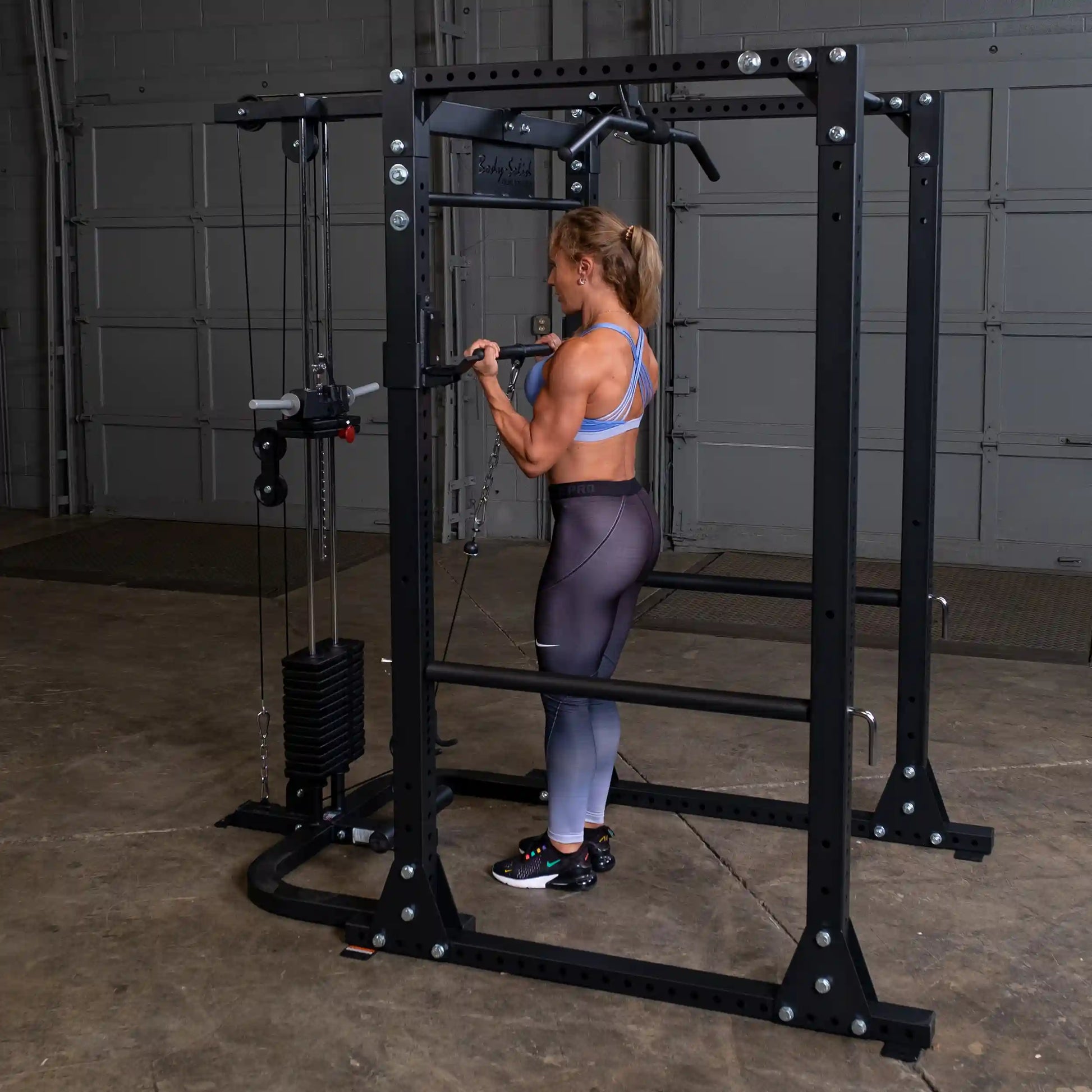 Woman using Body-Solid power rack for strength training in a gym.