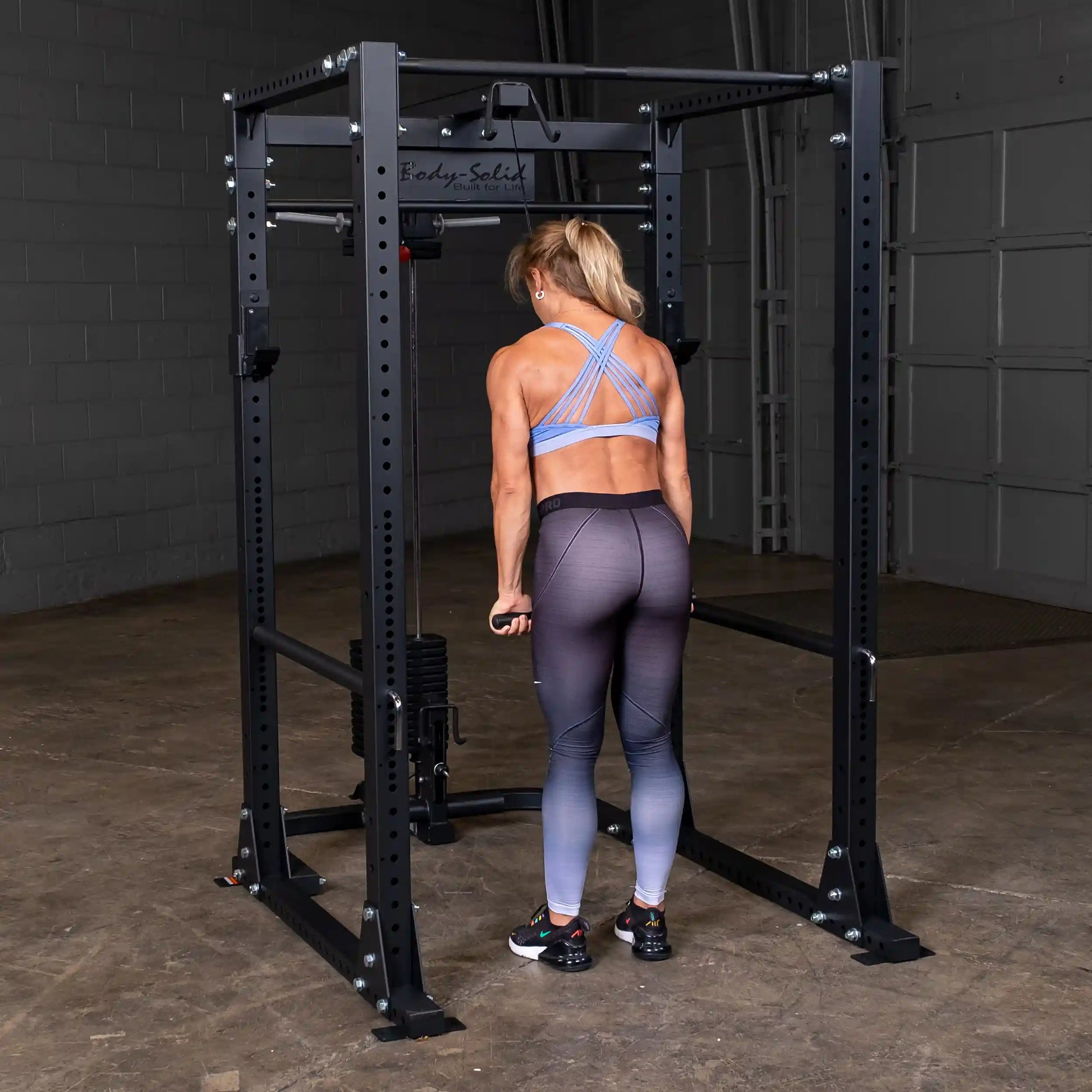 Woman using Body-Solid power rack in blue sports bra for strength training.