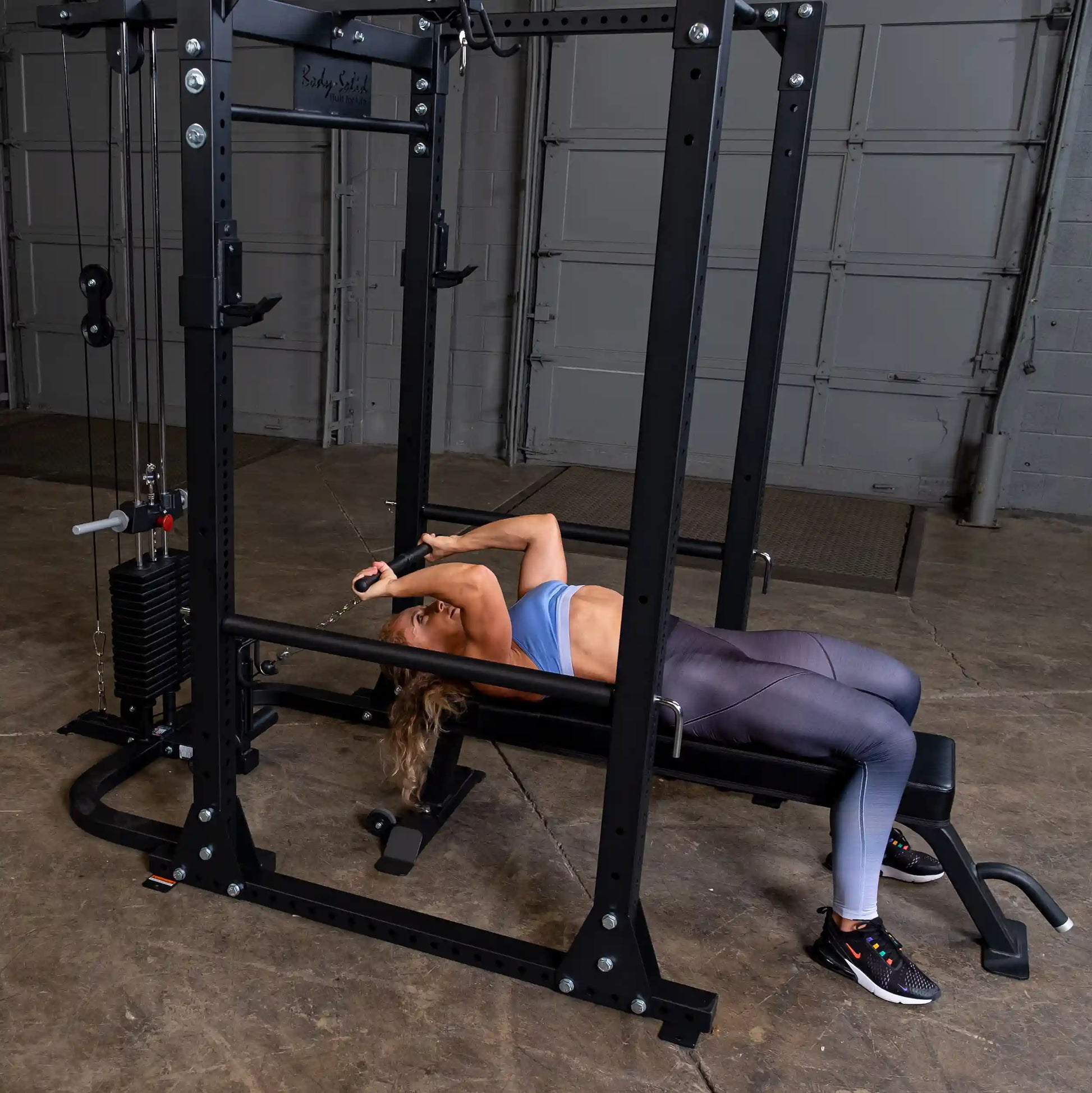 Woman using Body-Solid cable machine for bench exercise in gym.