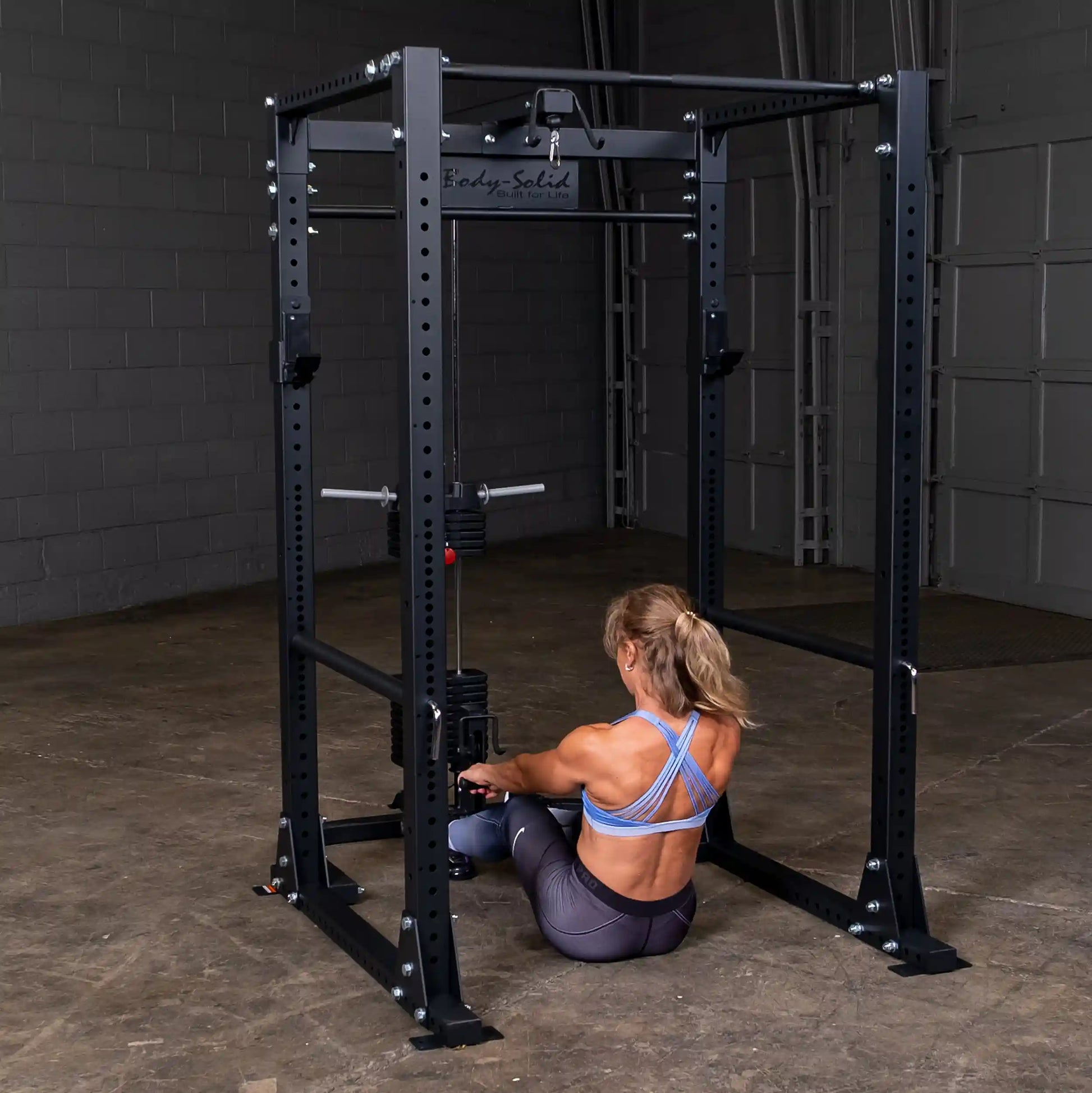 Woman using Body-Solid power rack with a cable machine in a gym setting.