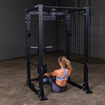 Woman using Body-Solid power rack with a cable machine in a gym setting.