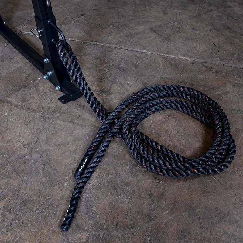 Black battle rope attached to gym equipment on concrete floor.