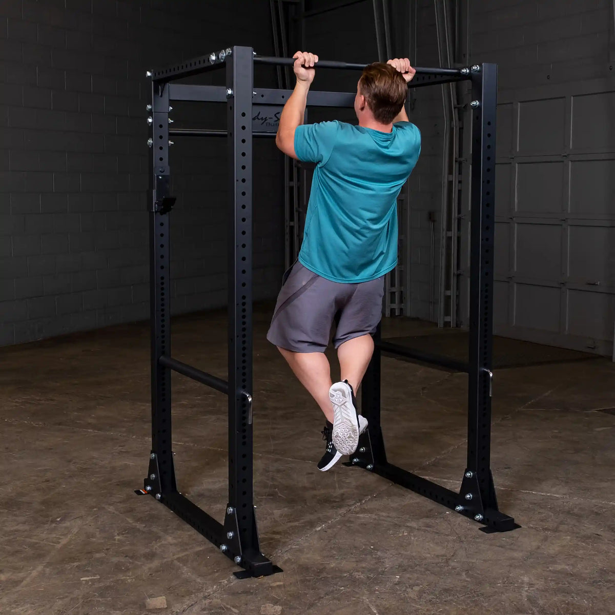 Man doing pull-up on black steel power rack in gym.