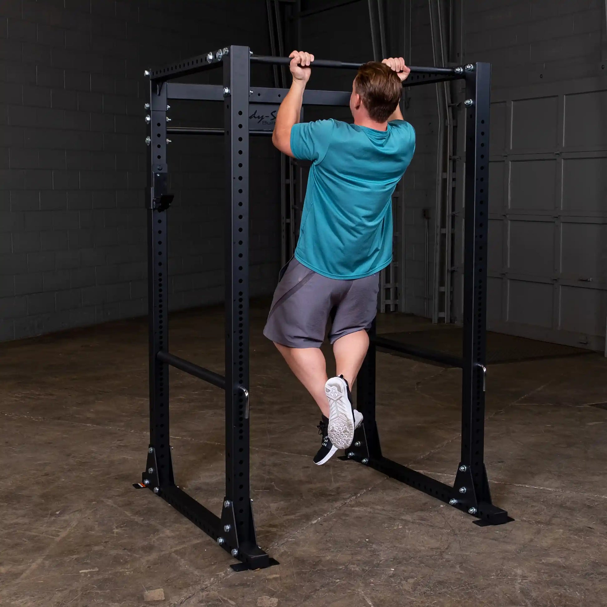 Man doing pull-up on black steel power rack in gym.