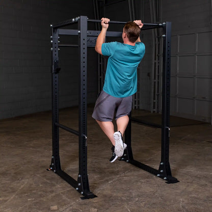 Man doing pull-up on black steel power rack in gym.
