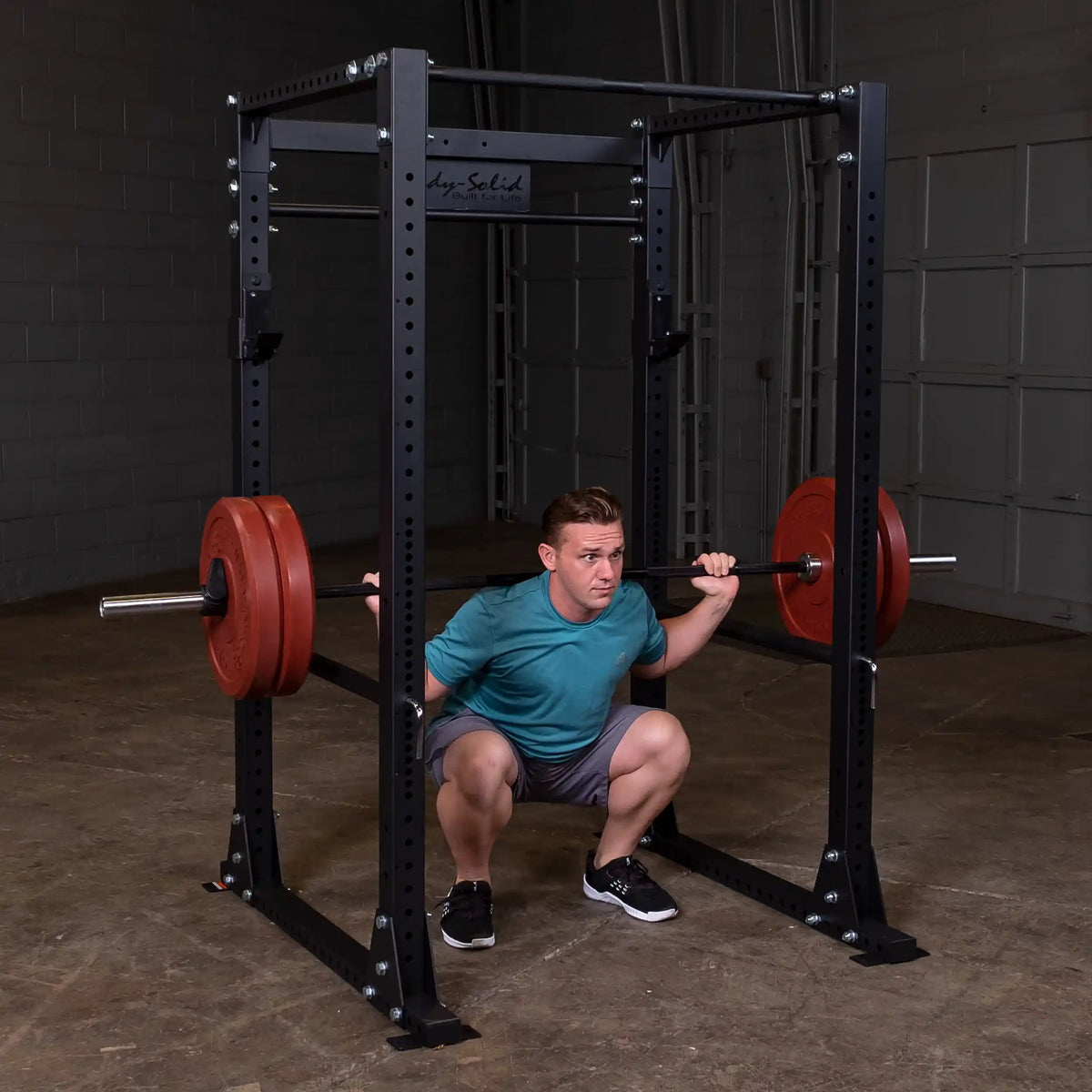 Man squatting with red weights on a Body-Solid power rack in a gym.
