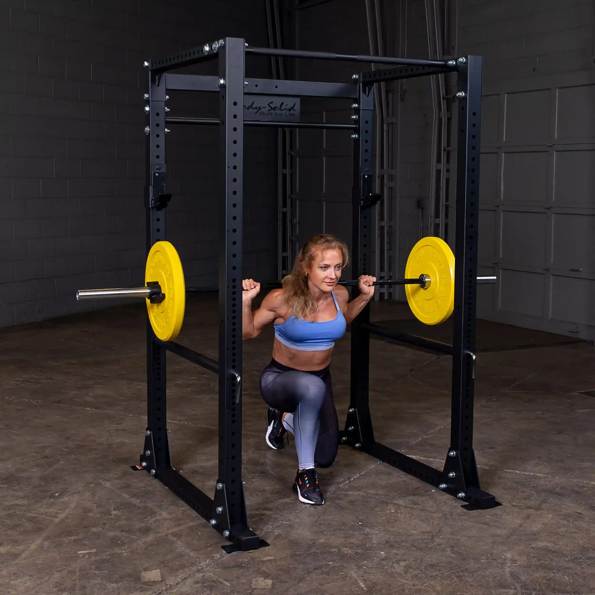 Woman performing squat in Body-Solid power rack with yellow weight plates.