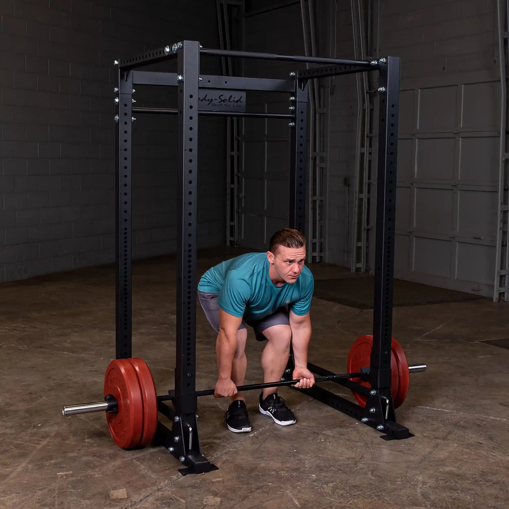 Man lifting barbell in Body-Solid power rack with red weight plates in gym.