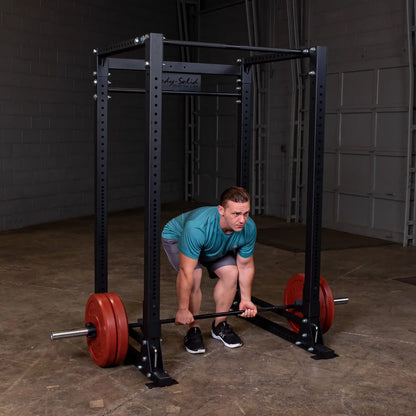 Man lifting barbell in Body-Solid power rack with red weight plates in gym.
