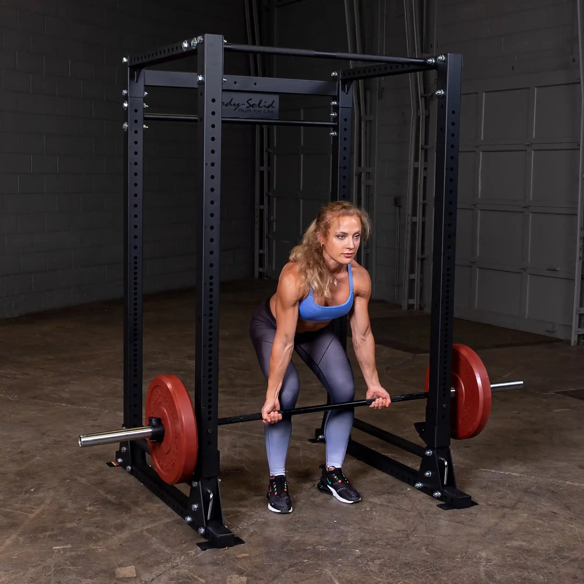Woman performs deadlift with red weight plates on Body-Solid power rack in gym.