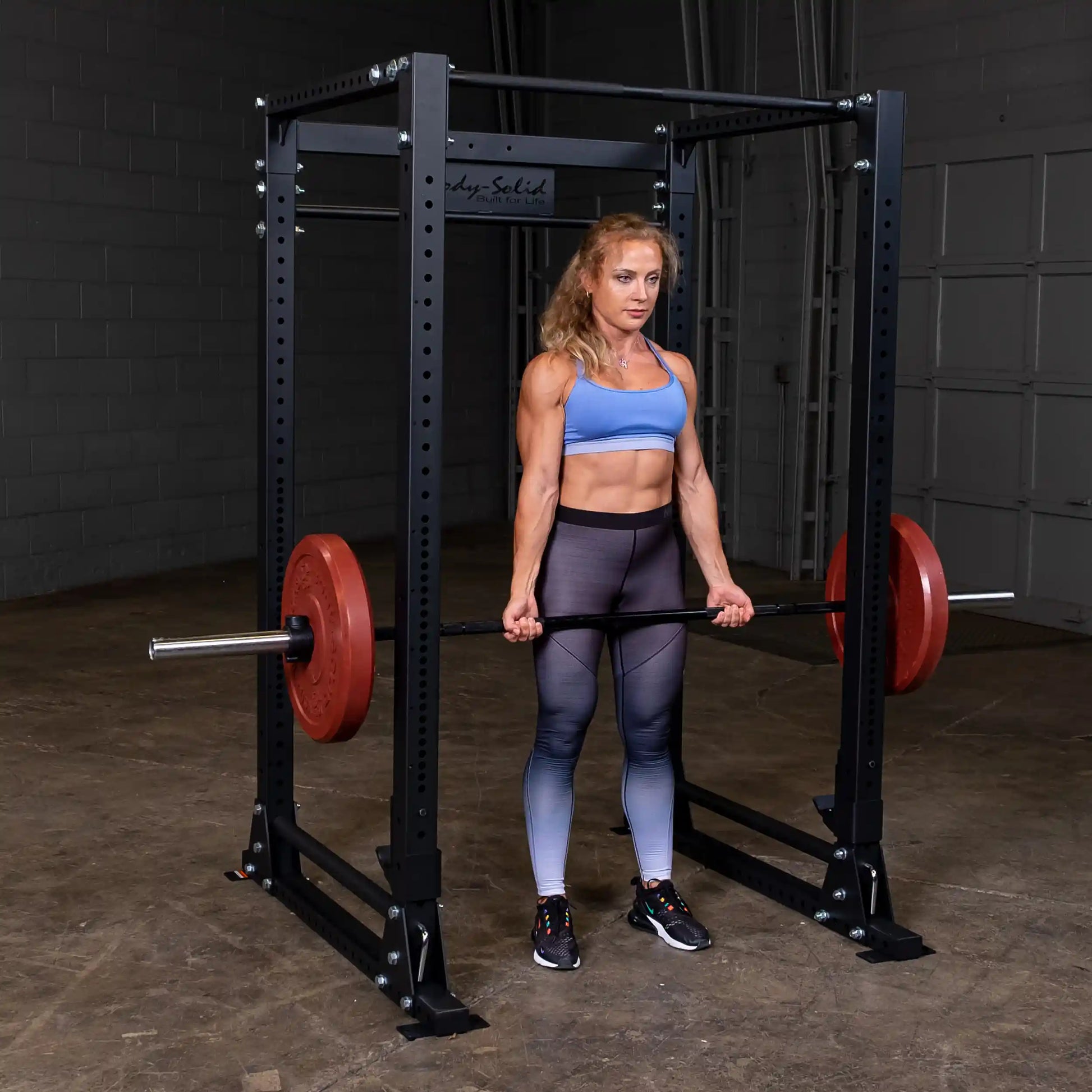 Athlete in blue top deadlifting with red weights in Body-Solid power rack.