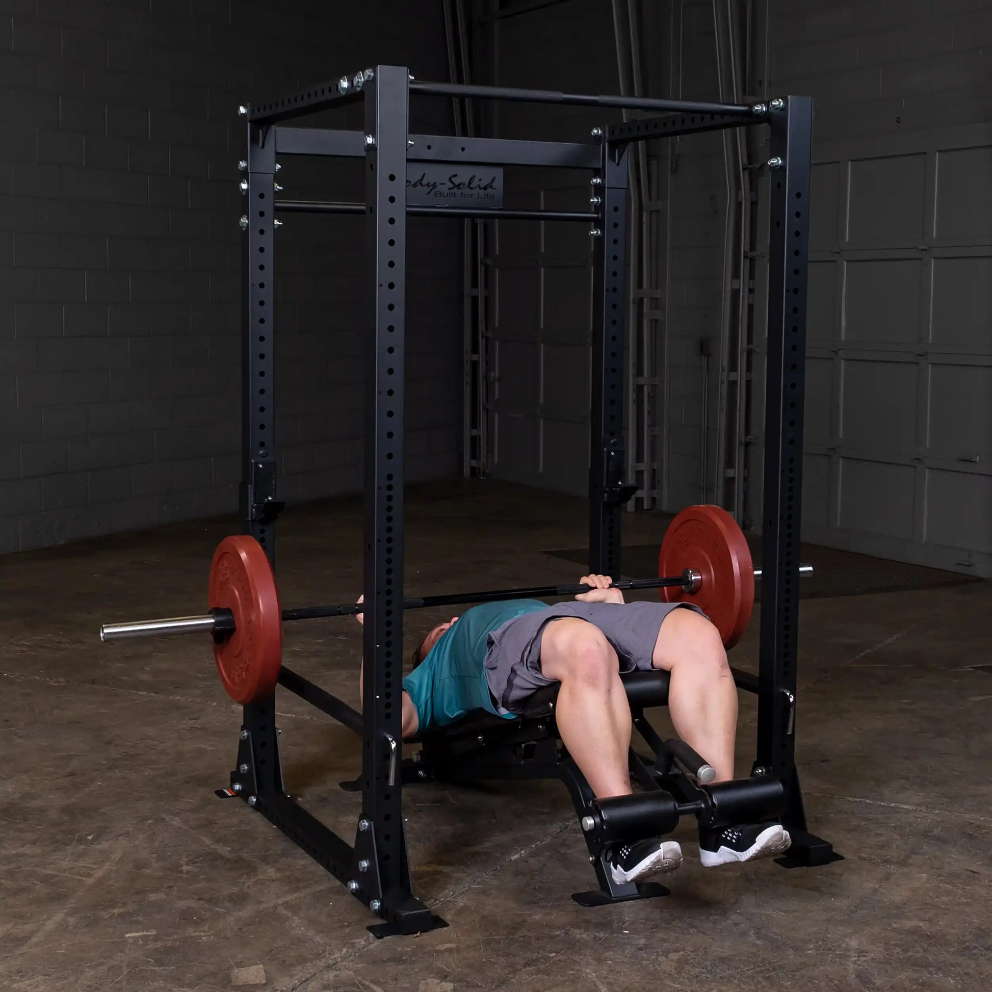 Man lifting weights on Body-Solid power rack with red plates in a gym.