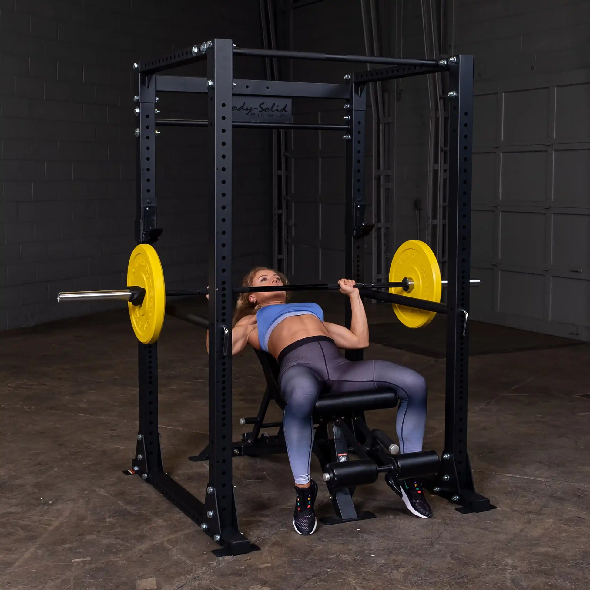Woman bench pressing in Body-Solid power rack with yellow weight plates.